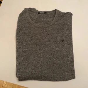 Grå tröja från J.Lindeberg - Snygg grå tröja från J.Lindeberg med rund halsringning. Perfekt för en stilren look. Den har en diskret logga på bröstet och är tillverkad i ett mjukt material.