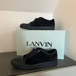 Svarta Lanvin skor  - Snygga svarta sneakers från Lanvin i mocka med snörning. Perfekta för en stilren look. Skorna har en diskret design med en solid svart färg och en robust sula.skorna så du kommer få många komplimanger av och ett para skor som tjejerna tycker om dom passar också vid en festkväll eller bara en vanlig dag.