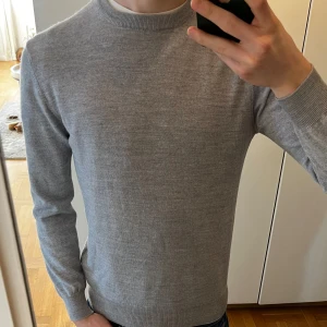 Grå merino tröja Moss London - Säljer en stilren grå tröja från Moss London, tillverkad i Italien. Tröjan är gjord av en blandning av merinoull och akryl, vilket ger en mjuk och bekväm känsla. Perfekt för kyligare dagar med sin klassiska design och långa ärmar. Storleken säger M men skulle säga att den passar S bättre. Hör gärna av vid frågor, funderingar eller prisförslag.