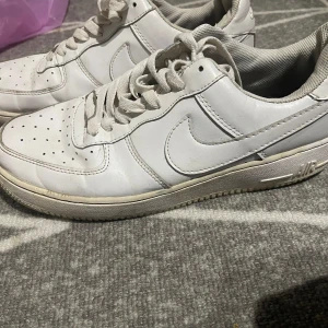 Vita Nike sneakers - Säljer ett par klassiska vita Nike sneakers med snörning. Perfekta för en stilren look. Skorna har en enkel och tidlös design med perforerade detaljer för ventilation.