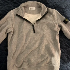 Grå tröja från Stone Island Junior - Säljer en stilren grå tröja från Stone Island med dragkedja vid halsen och det ikoniska märket på ärmen. Perfekt för en avslappnad och trendig look.