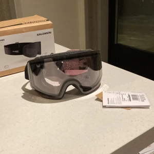 Skidglasögon Sentry Prime från Salomon - Snygga skidglasögon från Salomon, modell Sentry Prime. De har en svart ram med en justerbar rem i rosa och svart mönster. Glasögonen kommer med två utbytbara linser, en klar och en rödtonad, samt ett praktiskt fodral för förvaring. Magnet lins, väldigt enkelt att byta lins. Helt nya 10/10 skick. Ny pris 2600kr passa på att få ett kap