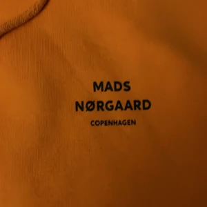 Orange hoodie från Mads Nørgaard - Säljer en snygg orange hoodie från Mads Nørgaard. Den har en klassisk design med dragsko i huvan och en praktisk magficka. Perfekt för en avslappnad stil.