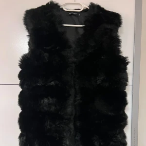Svart pälsväst  - Säljer en snygg svart pälsväst. Västen är perfekt för att hålla dig varm och stilren under kyligare dagar. Den har en mjuk och fluffig textur som ger en lyxig känsla. Passar perfekt över en tröja eller klänning.