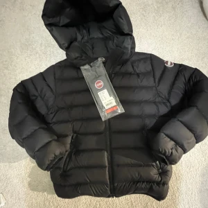 Svart dunjacka från Colmar - Säljer en svart dunjacka från Colmar med huva och dragkedja. Helt ny med prislapp på. Köpt på Nk i Stockholm för 4449kr ca en vecka sen. Säljer pga fel storlek. Tryck gärna på köp nu!💕