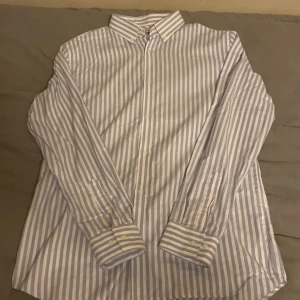 Jack & Jones skjorta - Säljer en stilren randig skjorta från Jack & Jones i storlek L. Skjortan är vit med blå ränder och har långa ärmar. Den är tillverkad i ett non-iron material vilket gör den lättskött och perfekt för en snygg look utan krångel. Knappar framtill och klassisk krage.
