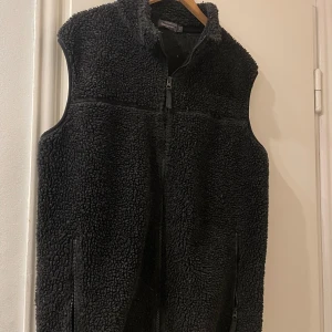 Svart fleeceväst från Dressmann - Säljer en svart fleeceväst från Dressmann i storlek L. Skönt material. blandning av akryl, polyester och ull. Mycket bra skick, säljer då den inte passar