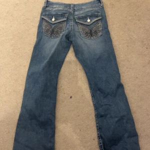 True religion Jeans - Snygga blå jeans med unika broderade detaljer på bakfickorna. De har en klassisk femficksdesign och en knappgylf. Köpt på Ginatricot med inga defekter på💕