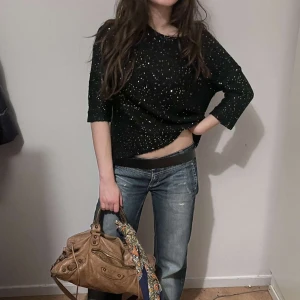 Svart glittrig tröja - Snygg svart tröja med glittriga detaljer. Tröjan har trekvartsärmar och en bekväm passform. Perfekt för att lägga till lite glitter i vardagen eller till en utekväll.