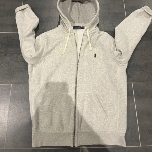 Ralph Lauren zip hoodie - Säljer en stilren grå hoodie från Ralph Lauren med dragkedja och klassisk logga på bröstet🤩. Den är i ett utmärkt skick och inget fel på den! Med mera frågor är de bara att skriva🙌🤝