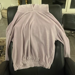 Ljuslila velour hoodie - Mysig ljuslila hoodie i velour med texten 'New Day' broderad på ärmen. Tröjan har en avslappnad passform med elastisk nederkant och muddar. Perfekt för en bekväm och stilren look.