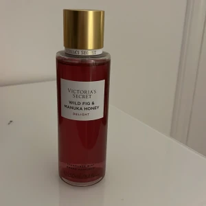 Victoria's Secret Wild Fig & Manuka Honey Delight - En lyxig parfym från Victoria's Secret med doft av vild fikon och manukahonung. Flaskan är elegant med en gyllene kork och rödtonad vätska. Perfekt för den som älskar söta och fruktiga dofter.