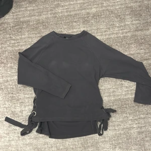 Svart långärmad tröja med snörning - Snygg svart långärmad tröja från Bikbok med coola snörningsdetaljer på sidorna. Perfekt för en avslappnad stil med en twist. Passar bra till jeans eller kjol för en trendig look.