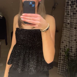 Svart glittrig tubtopp från Gina Tricot - Snygg svart glittrig tubtopp från Gina Tricot. Perfekt för en kväll ute med vänner. Toppen har en dragkedja på sidan för enkel på- och avtagning. Strl xs men passar mig som har strl s