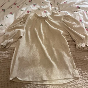 Beige blus med puffärmar - Säljer en stilren beige blus med puffiga trekvartsärmar och elastiska ärmslut. Perfekt för en elegant och avslappnad look.