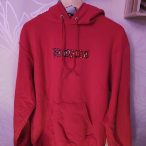Röd hoodie från Bronze - Säljer en cool röd hoodie från Bronze med tryck på framsidan. Den har en klassisk känguruficka och justerbar huva med dragsko. Perfekt för vardag och myskväll.