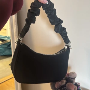 Svart axelväska med rynkad rem - Snygg svart axelväska med en unik rynkad rem och dragkedja upptill. Använd fåtal gånger