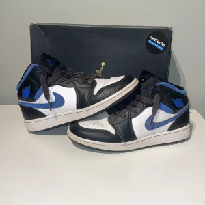 Nike Air Jordans 1 racer blue  - Snygga Nike Air Jordans i racer blue, med klassisk snörning. Perfekta för dig som älskar streetwear och vill ha en stilren look. Skorna har en ikonisk design med Nike-loggan i blått på sidan.