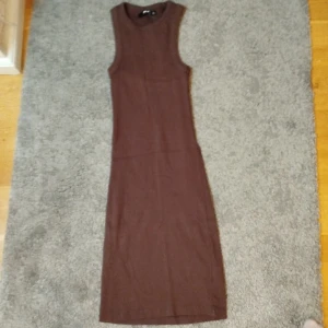 Brun fin sommarklänning  - Snygg brun ärmlös klänning i ribbat material. Den har en tight passform som framhäver figuren och är perfekt för en stilren look. Klänningen är knälång och passar bra till olika tillfällen.
