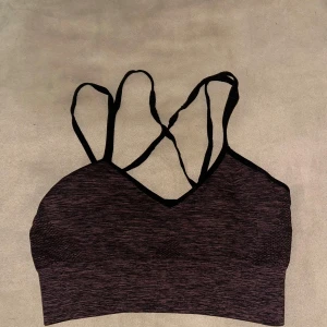 Grå och rosa sporttopp från In Motion - Säljer en grå och rosa sporttopp från In Motion med Quickdry-teknologi. Toppen har smala axelband och en snygg korsad ryggdesign. Perfekt för träning och andra aktiviteter.