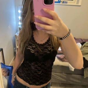 Svart spetslinne - Säljer ett snyggt svart spetslinne med vacker spetsdetalj. Linnet är ärmlöst och har en tight passform som framhäver figuren. Perfekt för en stilren look.