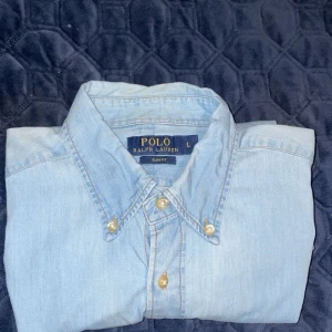 Ljusblå Ralph Lauren skjorta 👔  - Säljer en stilren ljusblå skjorta från Ralph Lauren i storlek L. Skjortan har en slim fit passform och är tillverkad i ett mjukt bomullsmaterial. Den har långa ärmar och knappar framtill samt en broderad logotyp på bröstet. Perfekt för en klassisk look! 9/10 skick!