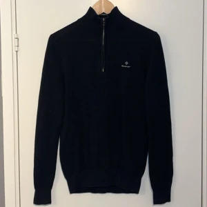 Svart Gant Half-Zip - Snygg svart tröja från Gant med halv dragkedja och diskret logga på bröstet. Tröjan har en klassisk design med långa ärmar och ribbade muddar. Perfekt för en stilren look. En defekt på höger arm går säker att fixa själv, Den är också lite urtvättad. Kom gärna med prisförslag MVH Elias🙌🏼