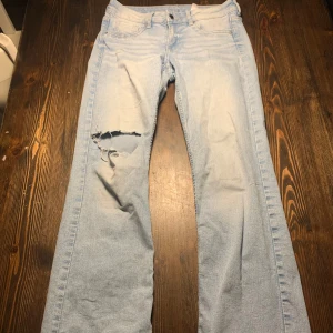 Ljusblå bootcut jeans - Säljer ett par ljusblå bootcut jeans i denim med låg midja. De har en snygg slitning på vänster ben. Knappt använda köpt på h&m