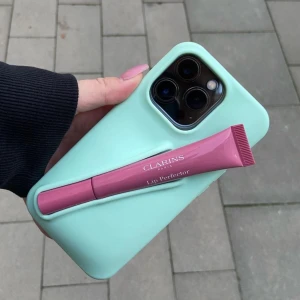 Mobilskal med läppglanshållare från Amore UF - Mobilskal med en hållare för läppglans eller andra skönhetsprodukter. Skalet är i färgen mintgrön till iPhone 13/14/15💓 Skalet rymmer flera olika sorters läpprodukter och ger ett bra skydd till mobilen🥰