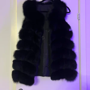 Svart äkta pälsväst - Snygg svart pälsväst som ger en lyxig känsla. Perfekt för att höja stilen på din outfit. Västen är fluffig och har en elegant design.  ordinarie pris 3000