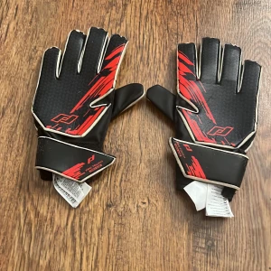 Svarta och röda handskar med vit insida - Snygga svarta handskar med röda detaljer och vit insida. Perfekta för sportaktiviteter med bra grepp och justerbar handledsrem. Designen är modern och stilren.
