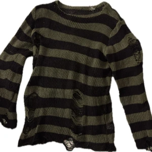 Randig stickad tröja - Säljer en cool randig stickad tröja i svart och olivgrön. Tröjan har en unik design med slitna detaljer och långa ärmar. Perfekt för en avslappnad och trendig look.