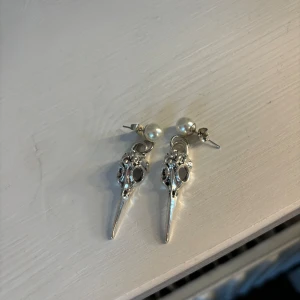 Örhängen med pärlor och dödskallemotiv - Unika örhängen med en kombination av pärlor och dödskallemotiv i silver, guldbilden är från hemsidan! Från smycka gbg och är aldrig använda