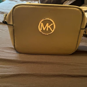 Rosa axelväska - Snygg rosa axelväska med guldfärgad logotyp på framsidan. Väskan har en kedjedetalj på axelremmen och en praktisk dragkedja för säker förvaring. Perfekt för att ge din outfit en lyxig touch.