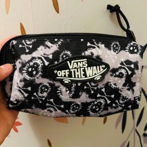 Svart och vit mönstrad plånbok från Vans - Säljer en cool plånbok/pennfoderal från Vans med deras ikoniska 'Off The Wall'-logga. Den har ett unikt svart och vitt mönster som ger en edgy look. Den har en dragkedja för extra säkerhet. Perfekt för vardag.