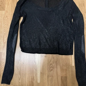 Tröja från Emporio Armani - I fint skick. Svart glittrig tröja med stor halsringning. Dragkedja bak och skinnimmitation på armbågar.