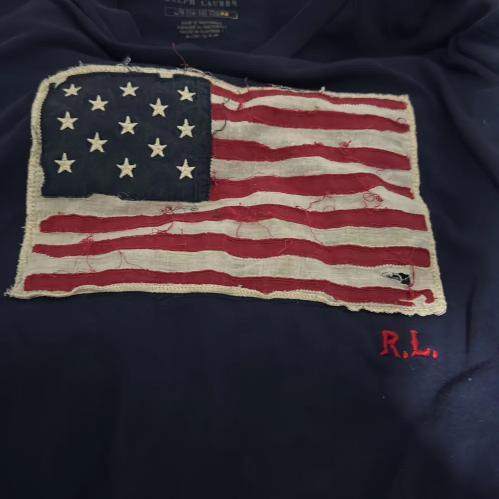 Säljer en snygg mörkblå t-shirt från Ralph Lauren med en cool amerikansk flagga på framsidan. T-shirten är i bomull och har korta ärmar. Perfekt för en avslappnad stil eller en somrig dag. Flaggan har en vintage-look med L barn är s i vuxen tror ja . T-shirts.