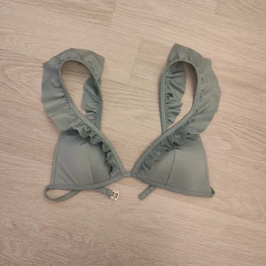 Bikini överdel - Jättefin bikini överdel med volang. Färgen är grön/grå. Justerbart spänne 