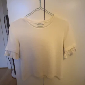 Vit stickad kortärmad tröja med volang - Jag säljer denna kortärmades stickade tröjan me volang i armen för att den inte kommer till så mycket användning längre