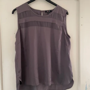 Grålila ärmlös topp från Yest - Säljer en stilren grålila ärmlös topp från Yest. Toppen har en enkel design med rund hals och är perfekt för både vardag och fest. Materialet känns lätt och luftigt, vilket gör den skön att bära under varmare dagar.