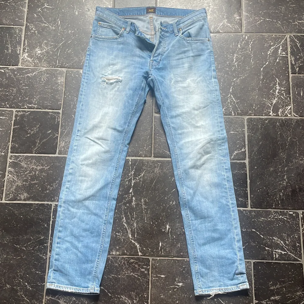 Säljer ett par ljusa jeans från Lee. De har en snygg slitning på ena benet och en klassisk femficksdesign. Jeansen är i en straight fit. Perfekta för en avslappnad stil!. Jeans & Byxor.