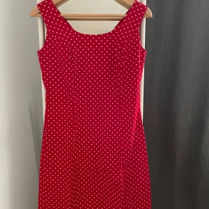 Röd prickig klänning - Säljer en superfin röd klänning med vita prickar. Den är ärmlös och har en klassisk, lite retro stil. Perfekt för sommarens alla fester eller en dag på stan. Klänningen är i nyskick och har en normal passform som sitter bekvämt. Den är gjord i ett lätt och skönt material, perfekt för varma dagar.
