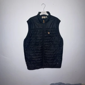 Fjällräven: ABISKO PADDED VEST - Nästa oanvänd Fjällräven väst i storlek XL men passar även L, fint skick och perfekt för hösten. Den har två extra innerfickor som du kan bevara småsaker i och två vägs dragkedja i mitten an västen. Ny pris 2000kr. Pris kan diskuteras 