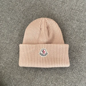 Ny beanie mössa i beige. Moncler liknande.  Modern, snygg, klassisk One Size - Helt ny mössa  Beanie mössa Moncler liknande .  Snygg, modern, populär.  Lika fin till vardags som vinteraktiviteter. 