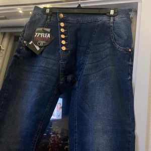 Mörkblå jeans från 77th Flea - Säljer ett par snygga mörkblå jeans från 77th Flea. De har en unik knappdetalj framtill med flera knappar i rad. Perfekta för en casual look eller att klä upp med en snygg topp. Obs! Färgen kan färga av sig, så var försiktig med ljusa plagg och möbler.
