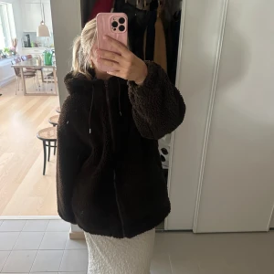 Mysig brun teddyjacka - Säljer en supermysig brun teddyjacka med dragkedja och huva. Perfekt för kyliga dagar. Jackan har långa ärmar och en avslappnad passform. Den är både varm och stilren, perfekt för höst och vinter! Storleken är 38 och den är i fint skick.