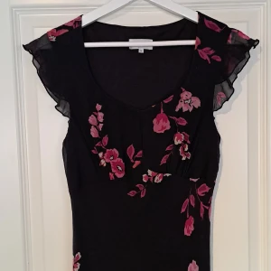 Lång blommig klänning - Asymetrisk lång klänning med rosa blommor och fina detaljer. Thriftad men i bra skick. Midi längd på mig som är 177. Storlek S. Från märket J & W.