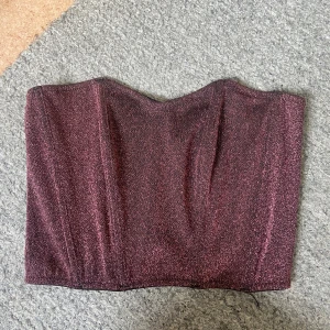 Glittrig vinröd korsett - Säljer en superfin glittrig vinröd korsett. Den är axelbandslös och har en snygg hakknäppning bak. Perfekt för festliga tillfällen när du vill sticka ut lite extra! ✨