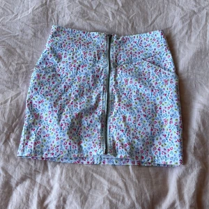 Blommig jeanskjol  - Kort jeanskjol med blommigt mönster. Dragkedja fram. Storlek 36 (säljer pga för liten)