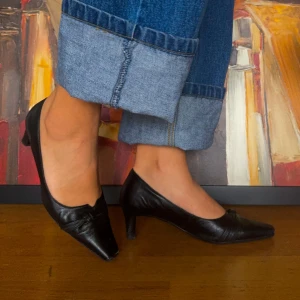 Svarta pumps med spetsig tå och rosett - Säljer ett par eleganta svarta pumps från Novita. De har en spetsig tå och en liten rosett framtill som ger en stilren look. Skorna är i skinn och har en låg klack, vilket gör dem bekväma att bära hela dagen. Perfekta för både kontoret och festlig!